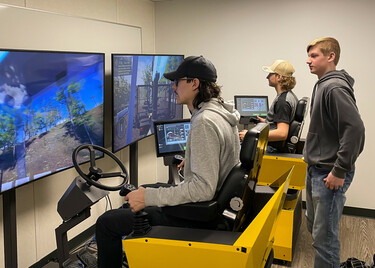high school students practicing driving earth moving equipment on electronic simulators